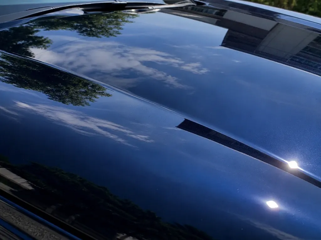 青空と木々を鮮明に映し込む艶のある車のボディ